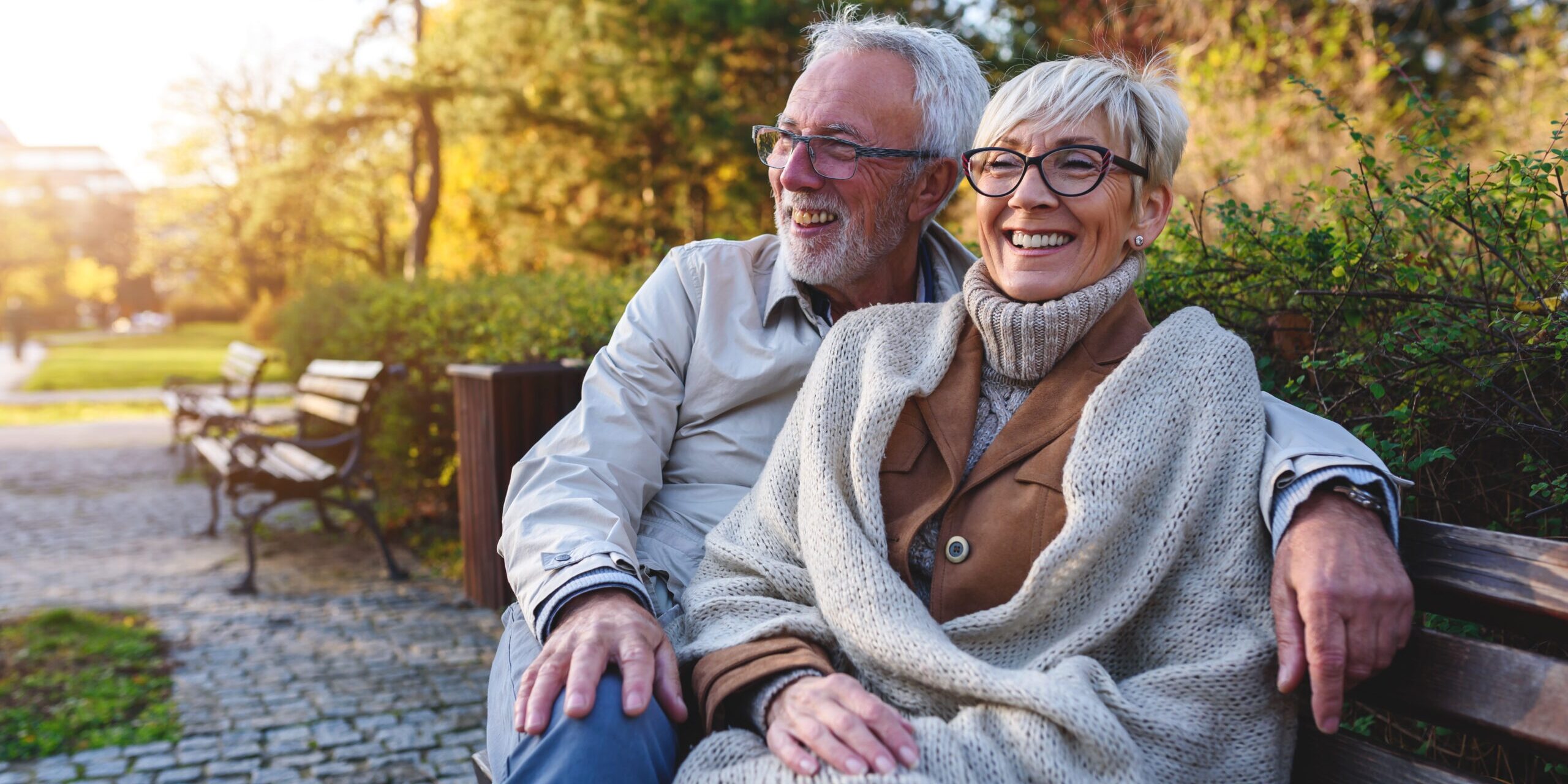 Smiling senior couple sitting on the bench in the park together Reverse Mortgage