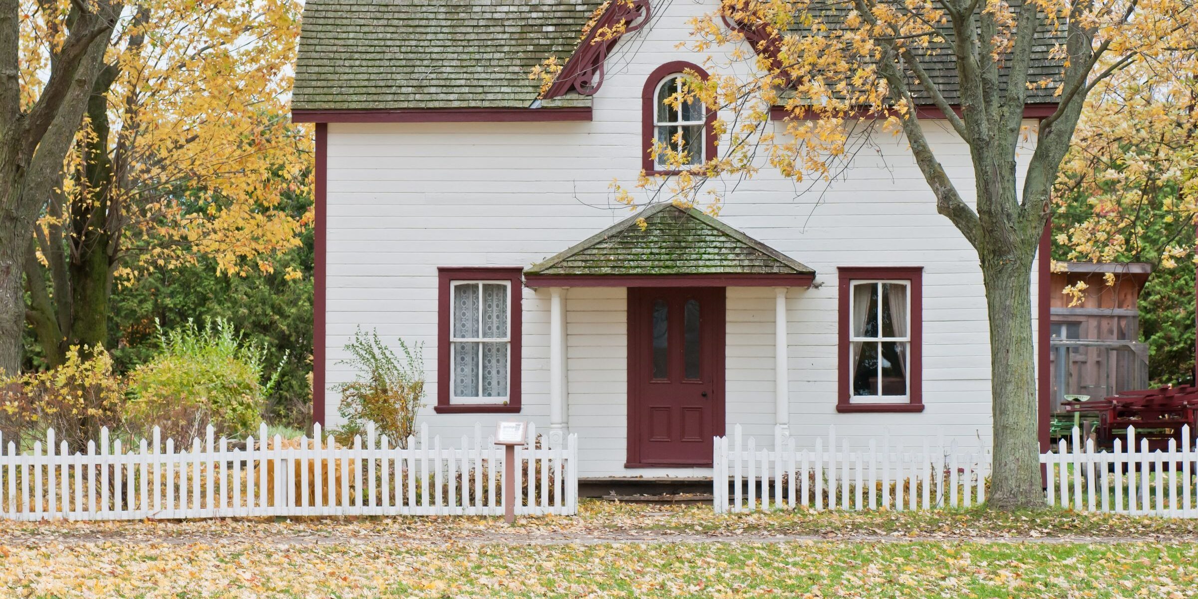 Classic white cottage with red trim and white picket fence — iconic first-time buyer home