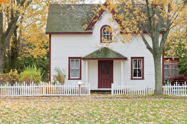 Classic white cottage with red trim and white picket fence — iconic first-time buyer home