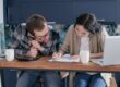 Young couple at kitchen table reviewing paperwork with a laptop and calculator, deciding how much house they can afford