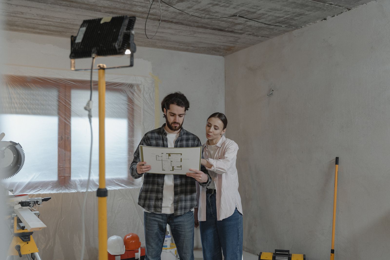 Young couple planning a home renovation project with blueprints, considering how to fund the remodel with a cash-out refinance