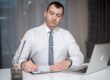 Focused professional at his desk writing refinance closing cost breakdown notes with laptop and paperwork, calculating the total cost to refinance a 300000 dollar mortgage
