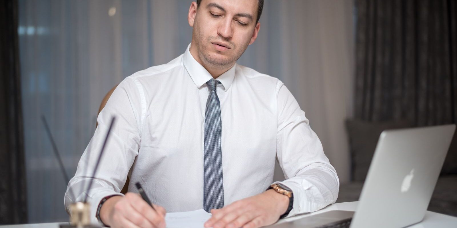 refinance-300k-mortgage-cost-breakdown-2026 Focused professional at his desk writing refinance closing cost breakdown notes with laptop and paperwork, calculating the total cost to refinance a 300000 dollar mortgage