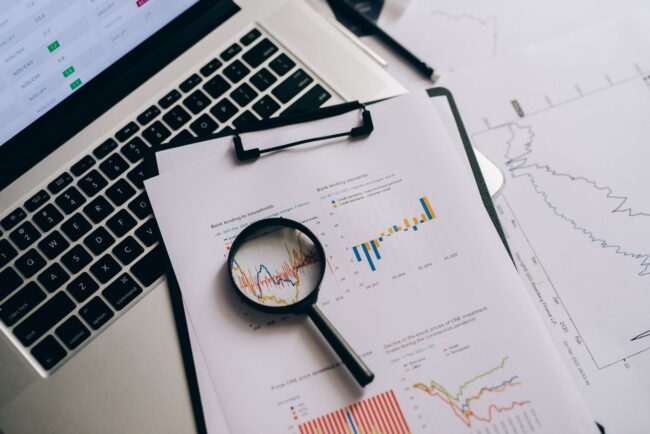 Overhead view of financial charts on paper with a laptop, magnifying glass, and analysis tools, previewing the September 2026 BLS Employment Situation Report ahead of Friday October 2 and its likely impact on mortgage rates