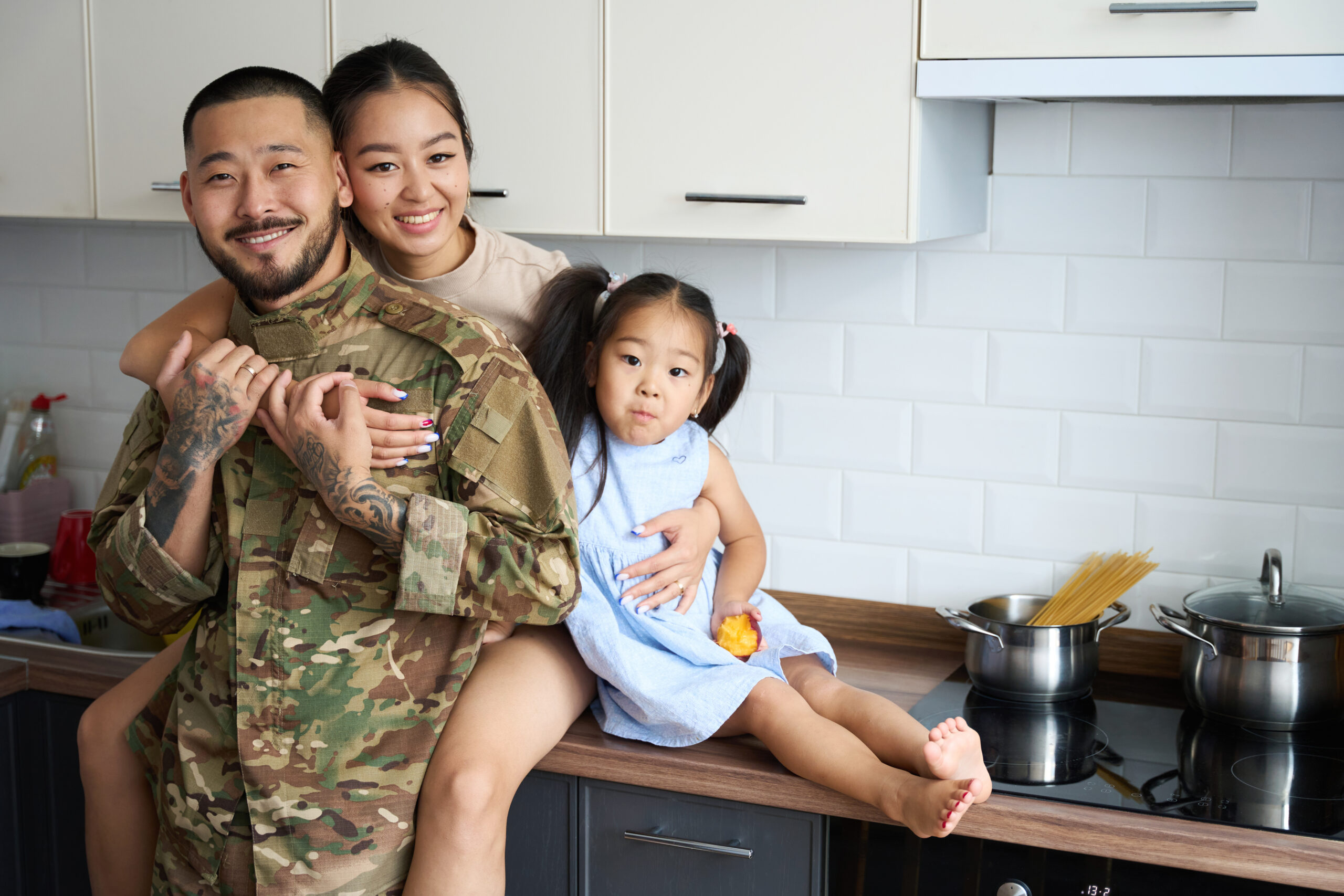 Asian American veteran with wife and young daughter in their home kitchen, illustrating family life savings a VA IRRRL refinance can deliver