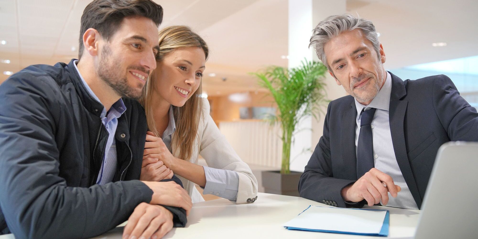 Couple meeting with a licensed mortgage broker at a modern office desk, reviewing OnPoint Zero to Hero Refinance two-option program details on a laptop to choose between par-rate no-lender-fees and lender-credit paths