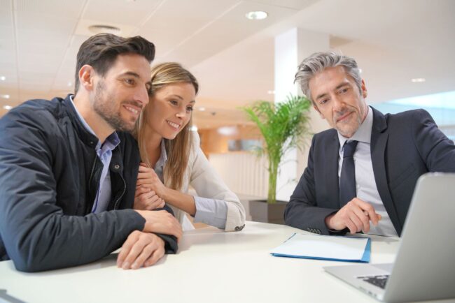 Couple meeting with a licensed mortgage broker at a modern office desk, reviewing OnPoint Zero to Hero Refinance two-option program details on a laptop to choose between par-rate no-lender-fees and lender-credit paths