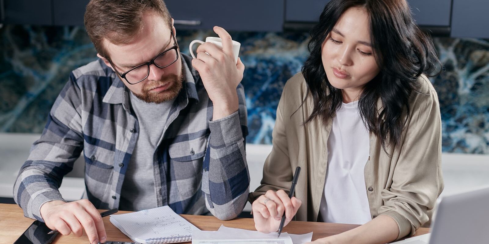 day01-income-needed-home-2026 Couple at their kitchen table running the household income and debt math with a calculator and laptop, determining what mortgage payment they can afford on a $500K, $750K, or $1M home in Orange County in October 2026